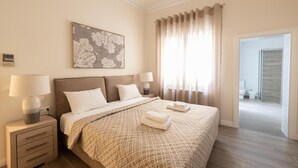 Hotellihuone, jossa on suuri sänky, kaksi yöpöytää valaisimineen, seinällä oleva kukka-aiheinen taideteos ja näkymä kylpyhuoneeseen avonaisen oven kautta.