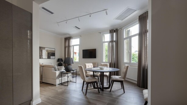 A modern living room with a sofa, a dining table with chairs, a flat-screen TV mounted on the wall, and large windows with curtains. - Plaka s Privileged Accommodation (Athens)