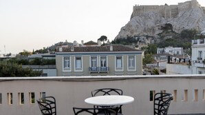 A terrace with a table and chairs, overlooking a historic building and a rocky hill. - Plaka s Privileged Accommodation (Athens)