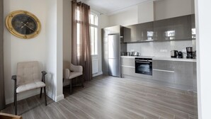 A modern kitchen with stainless steel appliances, a dining area with a chair, and a large wall clock. - Plaka s Privileged Accommodation (Athens)