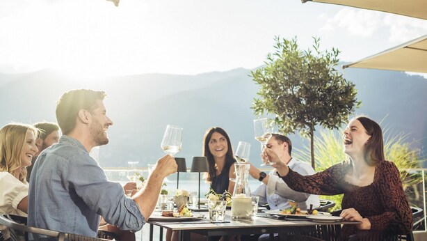 Un groupe de personnes est assis à des tables, entouré de chaises et protégé par des parasols, et prend son repas en plein air.