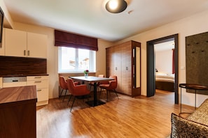 A modern kitchen with wooden cabinets, a dining table with chairs, and a large window with a view.