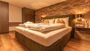Una cama bien tendida con toallas dobladas, una pared con textura de piedra y dos lámparas de noche.