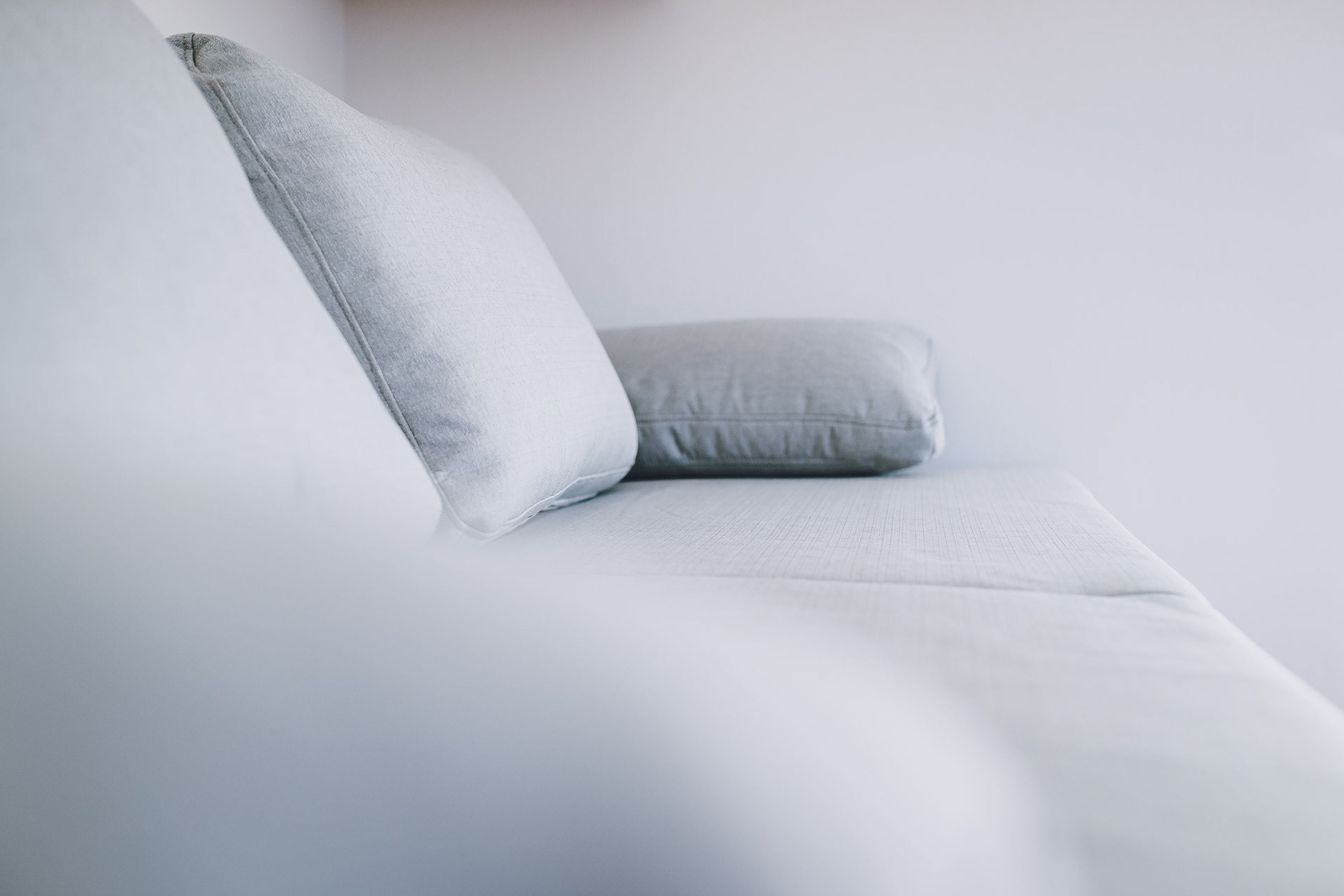 A white sofa with a light grey pillow.