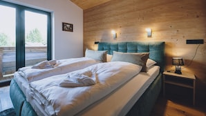 Une chambre avec un plafond en bois, un grand lit avec une literie blanche, deux lampes de chevet et une vue sur l’extérieur grâce à une grande fenêtre.