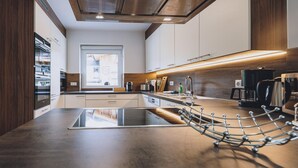 A modern kitchen with a central island, built-in appliances, and a wooden ceiling. - Spa Chalet - Garden Lodge (Zell am See)