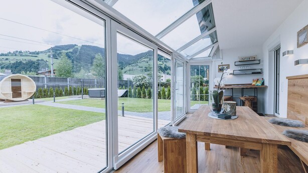 A modern kitchen with large windows, a wooden dining table, and a view of a green landscape. - Spa Chalet - Garden Lodge (Zell am See)