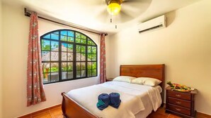 A bedroom with a wooden bed, a nightstand, a window with curtains, and a ceiling fan. - Casa 48· Poolside Relaxing Retreat Near the Beach (Esterillos Este)