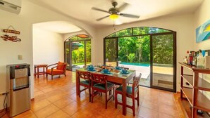 A dining area with a table set for four, a ceiling fan, and a view of a swimming pool through large glass doors. - Casa 48· Poolside Relaxing Retreat Near the Beach (Esterillos Este)