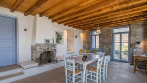 Et rustikt interiør med en stenspir, træbjælker i loftet, et spisebord med stole og en stenvæg.