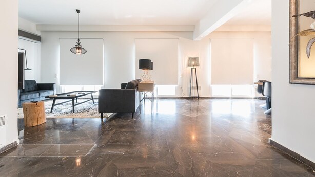 A spacious living area with a dark stone floor, a sofa, a coffee table, and a hanging light fixture. - Spacious 4BR Penthouse Updated Bathroom (Athens)