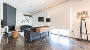 A modern living room with a dark marble floor, a grey sofa, a wooden coffee table, and a black floor lamp. - Spacious 4BR Penthouse Updated Bathroom (Athens)