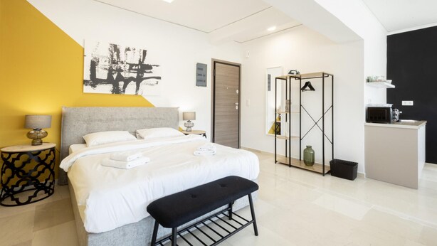 A modern bedroom with a bed, bench, bedside tables, a wardrobe, and a kitchenette. - Hip And Fun in Athens Apt A (Athens)