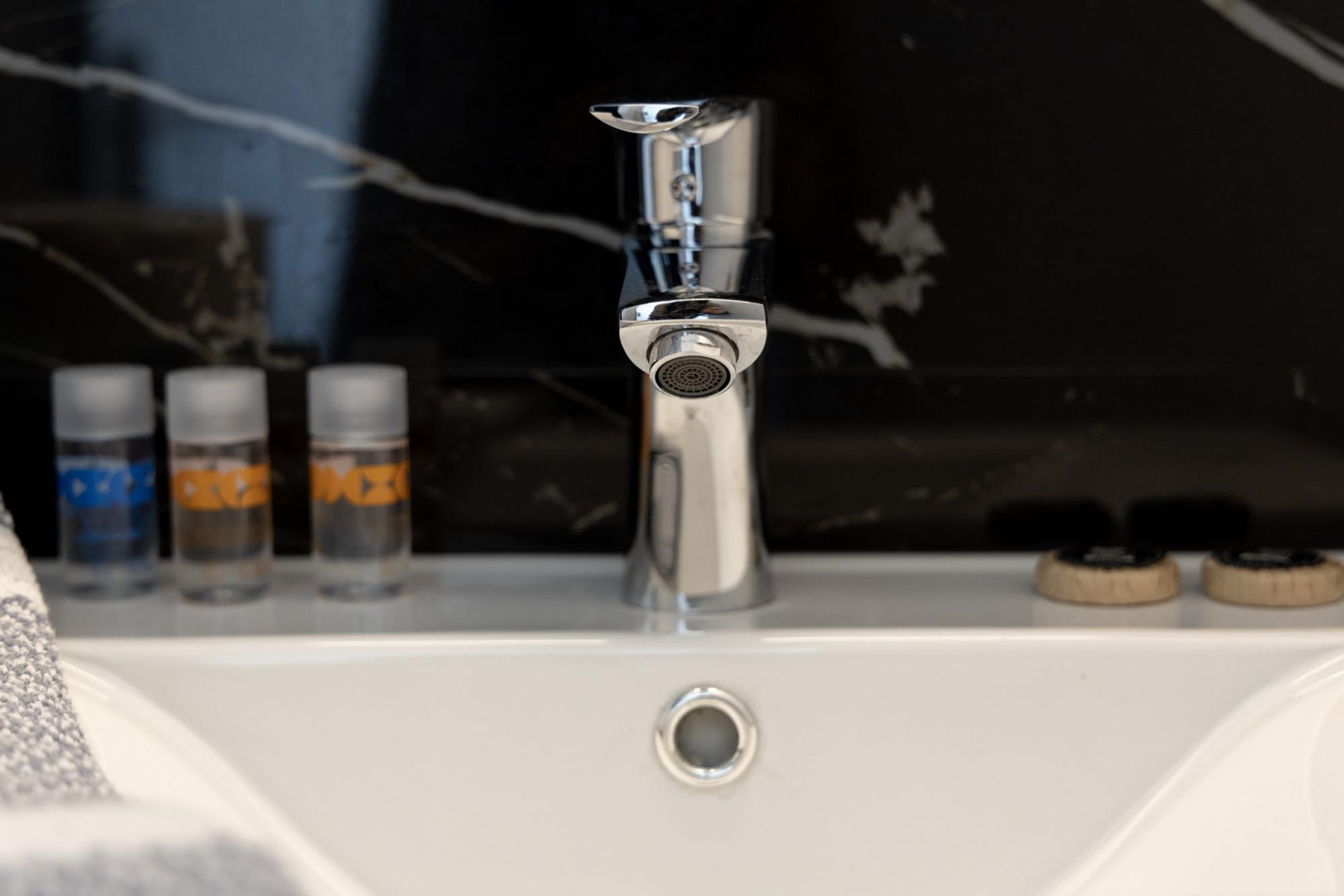 Un lavandino da bagno con un rubinetto cromato, uno specchio e tre flaconi di sapone.