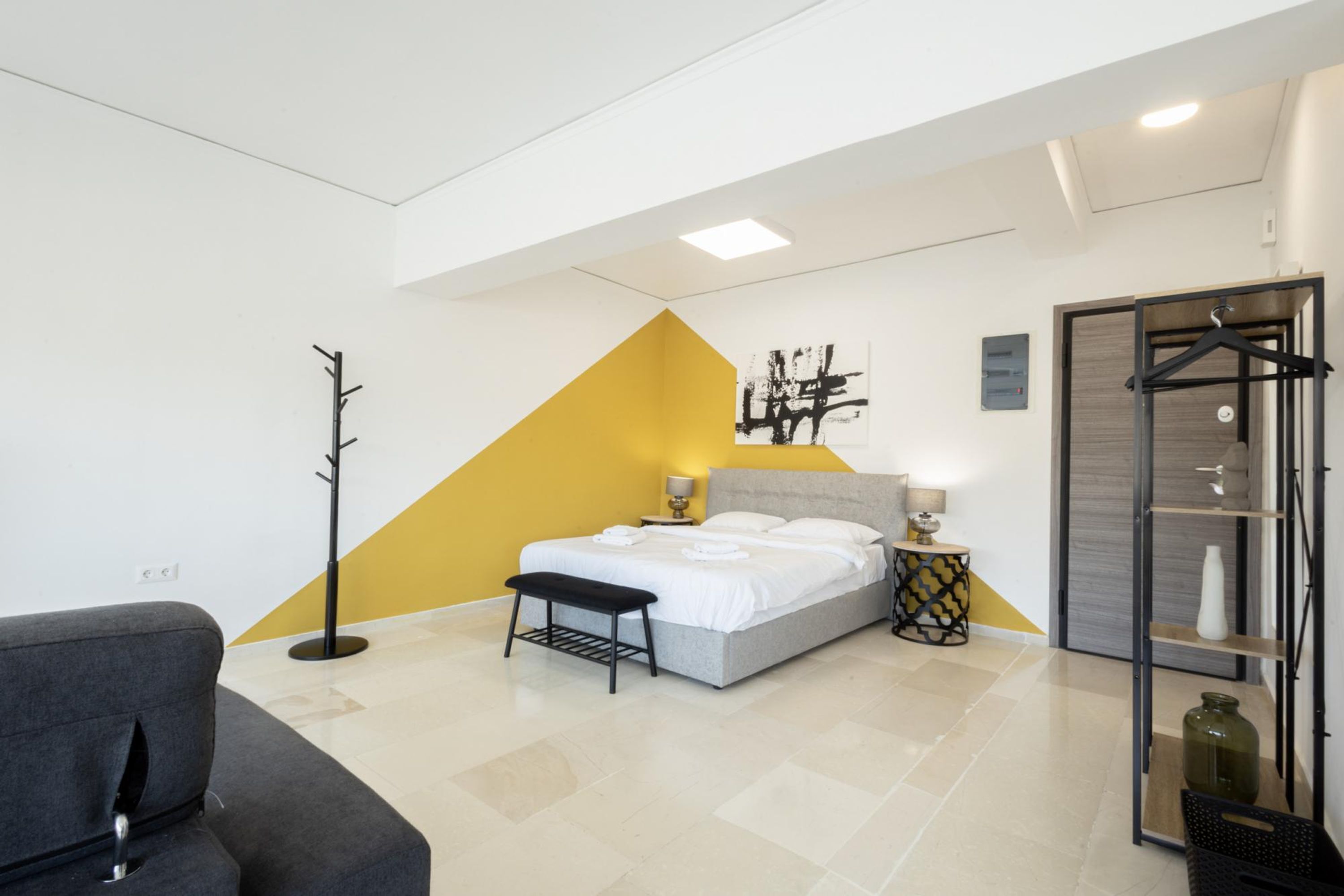A modern bedroom with a bed, bedside table, lamp, and a coat rack.