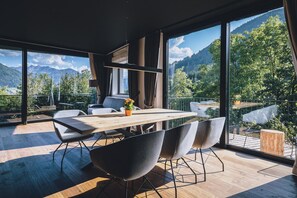 Un comedor moderno con mesa y sillas de madera, ventanas amplias con vistas a la montaña y un balcón con vistas al paisaje.