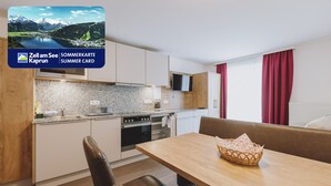 A modern kitchen with granite countertops, a built-in oven, and a microwave. There is a dining area with a wooden table and a wicker basket. - Appartements Sulzer - TOP 12 (Zell am See)