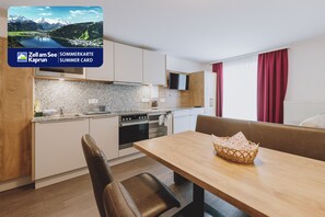 A modern kitchen with granite countertops, a built-in oven, and a microwave. There is a dining area with a wooden table and a wicker basket. - Appartements Sulzer - TOP 12 (Zell am See)
