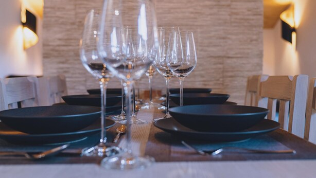 A dining table set with black plates, clear wine glasses, and a wooden table runner. - Premium Apartments Areit - Balcony (Zell am See)