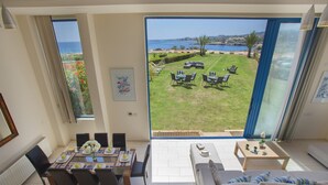 A spacious living area with a large sliding glass door leading to a private outdoor patio with a view of the sea. - Villa Infinite Aretousa (Paralimni)