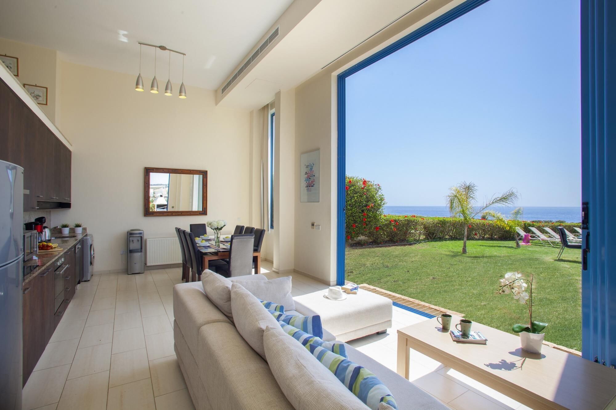 A modern living room with a large window overlooking a garden and the sea.
