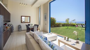 A modern living room with a large window overlooking a garden and the sea. - Villa Infinite Aretousa (Paralimni)
