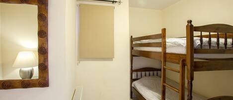 A small, single-bedded room with a wooden bunk bed, a bedside table with a lamp, a radiator, and a mirror with a decorative frame.