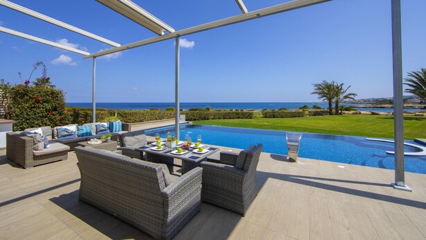 A poolside area with outdoor furniture, a table set with drinks, and a view of the sea. - Villa Infinite Aretousa (Paralimni)