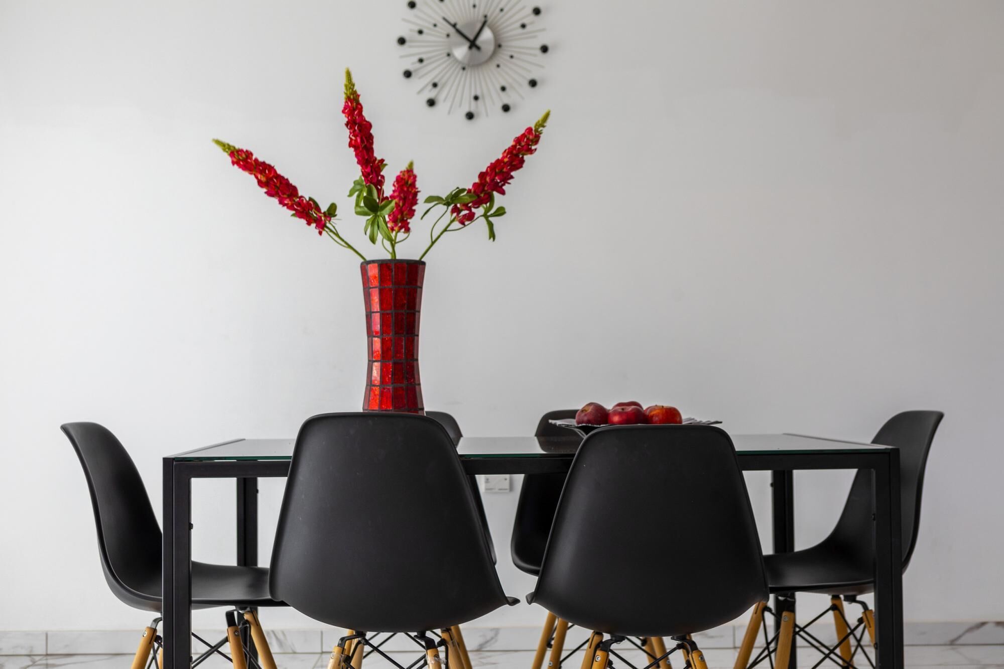 Een eettafel met een rode vaas, zwarte stoelen en een klok aan de muur.