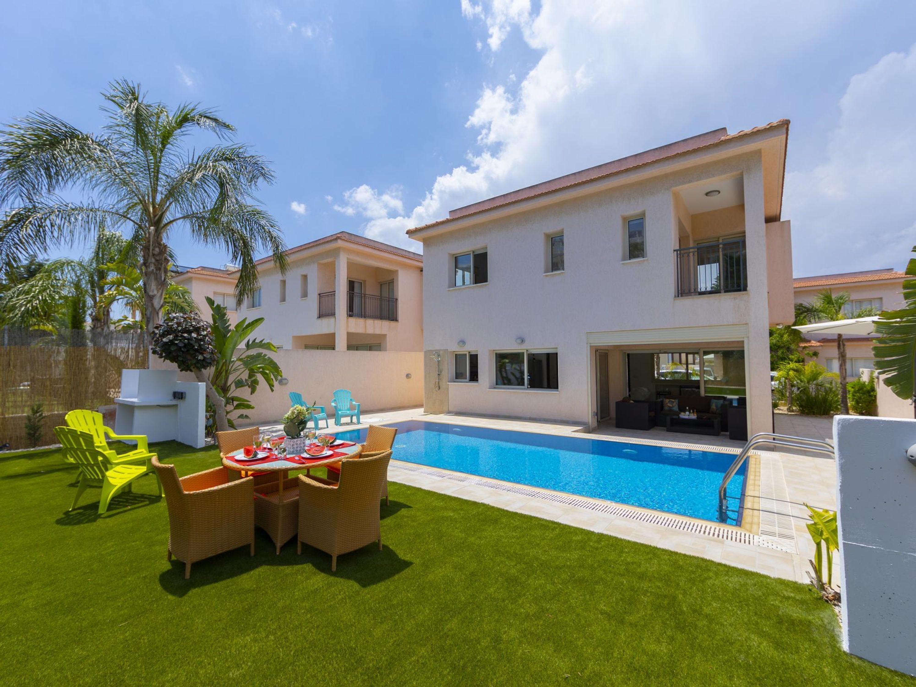 Una casa moderna de dos pisos con piscina, mobiliario exterior y un césped bien cuidado.