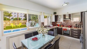 A modern kitchen with a dining area, large windows, and a view of a pool and greenery.