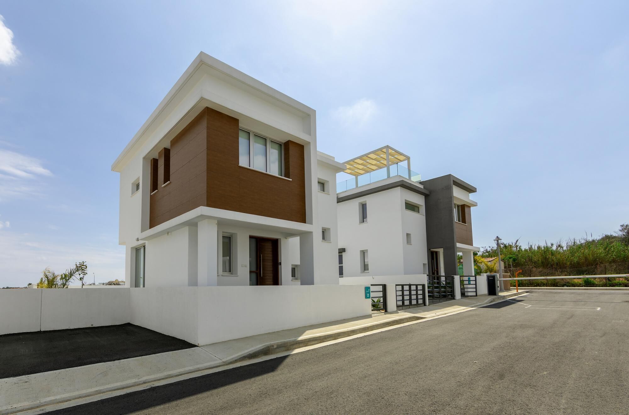 A modern two-story residential building with a flat roof, large windows, and a covered outdoor area.