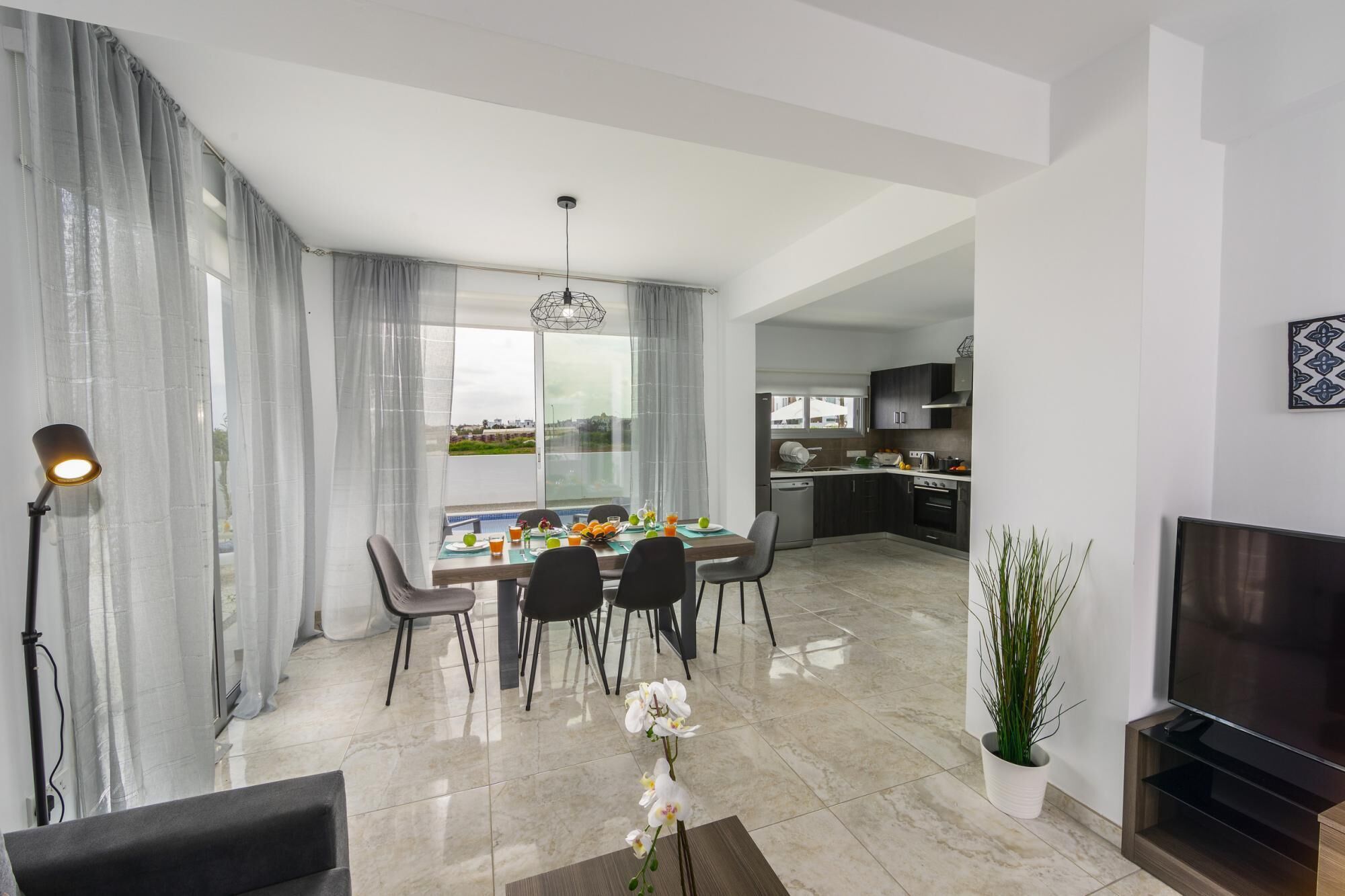 A modern dining area with a table set for four, a kitchen in the background, and a TV on the right.