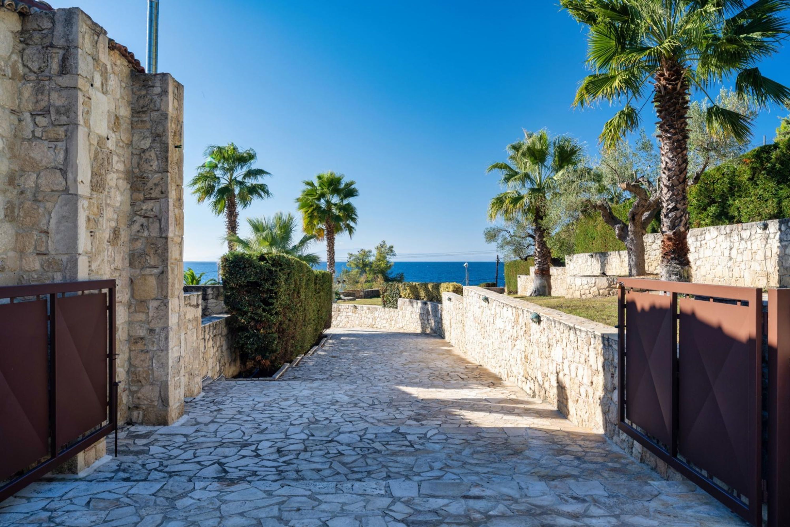 Un sendero de piedra que conduce a una zona vallada con palmeras y vistas al mar.