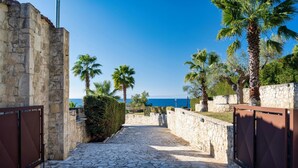 A stone pathway leading to a gated area with palm trees and a view of the sea. - Palmrise Luxury Villas - Thea Villa (Kassandra)