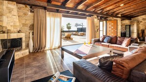 A spacious living area with a stone fireplace, wooden ceiling beams, and a view of the outdoors. - Palmrise Luxury Villas - Thea Villa (Kassandra)