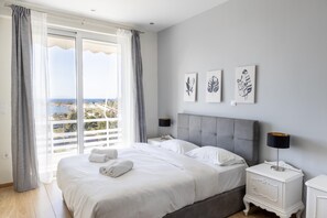 Relax in this serene bedroom with a large bed, grey headboard, and a view of the coastal landscape.
