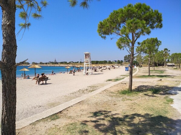 Guests can enjoy the beach with umbrellas providing shade, a lifeguard tower nearby, and scenic views of the surrounding trees.
