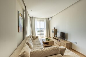 Relax in this stylish living room with a large sofa, flat-screen TV, and sliding glass door leading to a city view balcony.