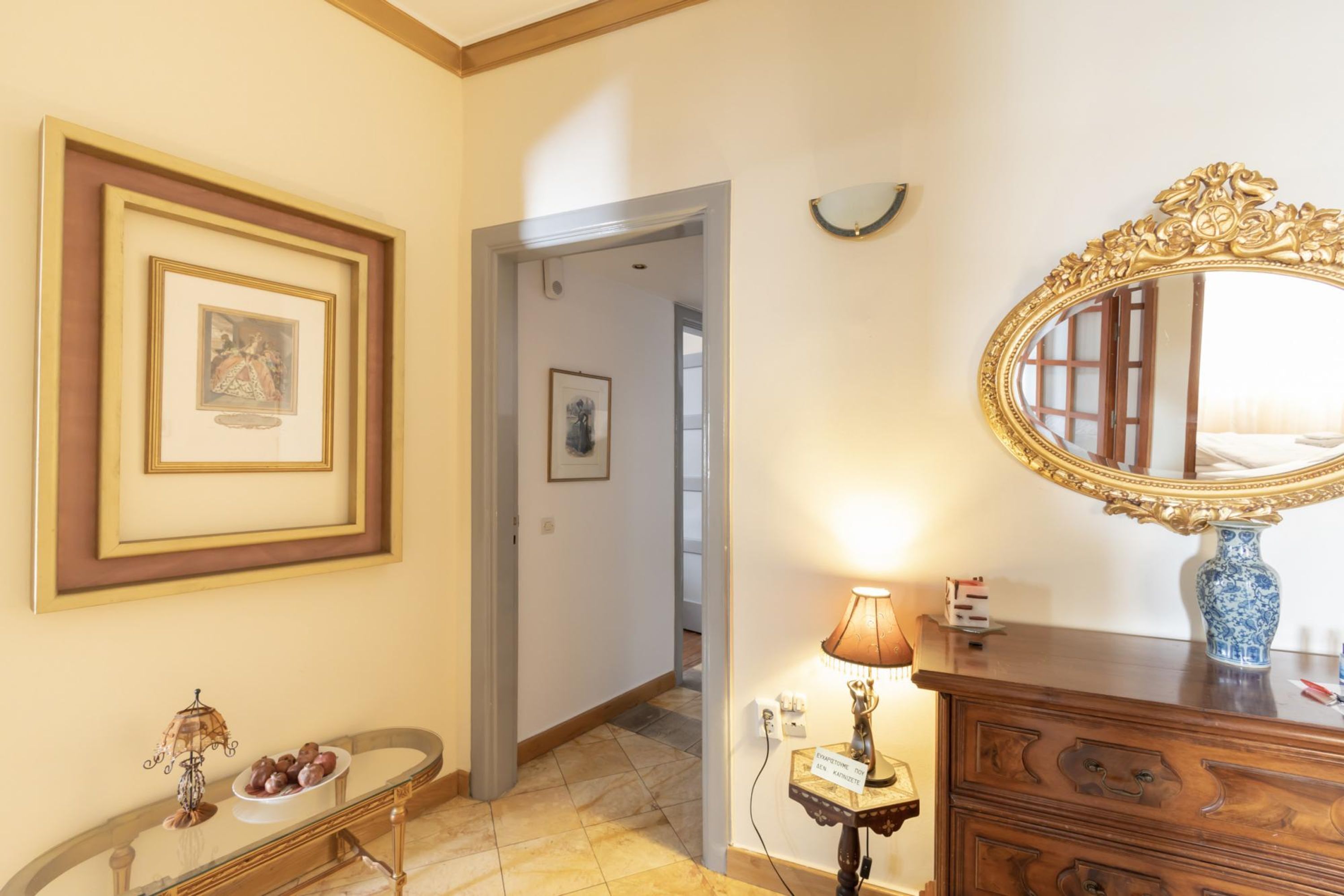 A hotel room with a framed picture, a mirror, a dresser, a lamp, and a console table with decorative items.