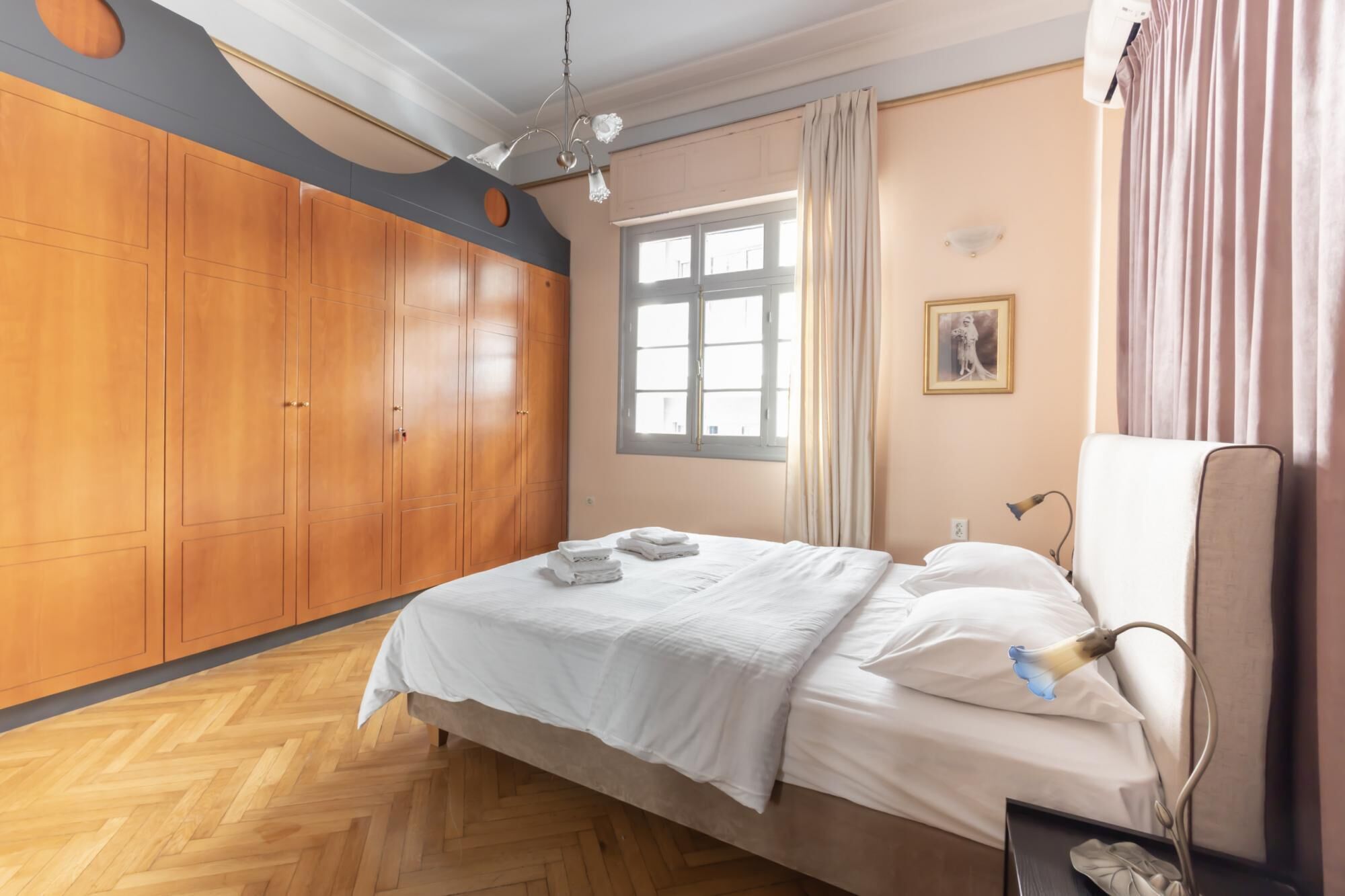 A bedroom with a bed, wooden wardrobe, window, and a nightstand with a lamp.
