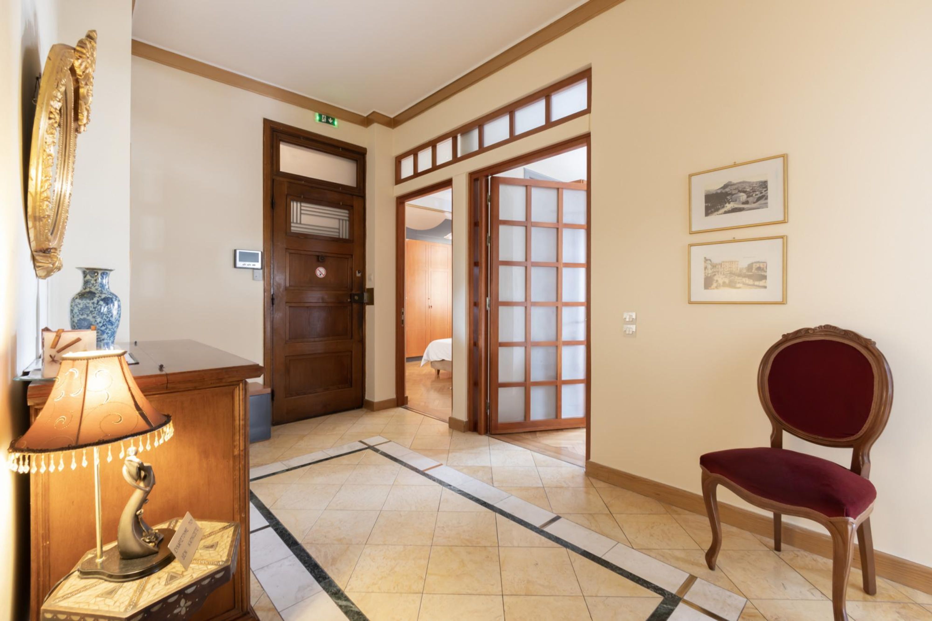 A hotel lobby with a wooden reception desk, a red chair, a traditional Japanese sliding door, and framed pictures on the wall.