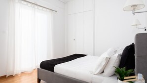 Een moderne slaapkamer met een bed, gordijnen, een nachtkastje met een lamp en een potplant.