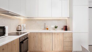 Een moderne keuken met witte kasten, een inbouwoven, een magnetron, een koffiezetapparaat en een gootsteen.