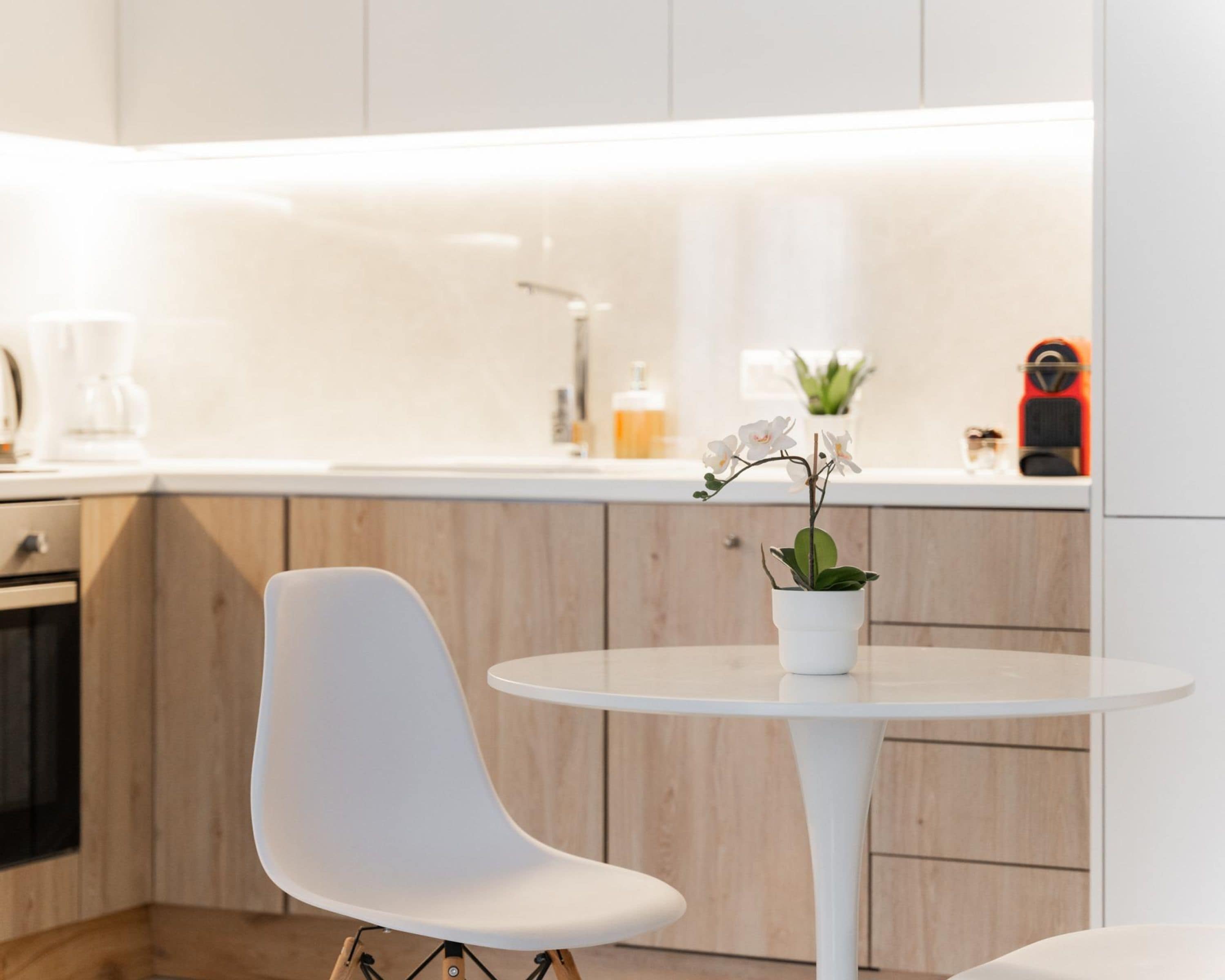 Une cuisine moderne avec des meubles en bois, un plan de travail blanc, une chaise blanche et une petite table sur laquelle est posée une orchidée en pot.
