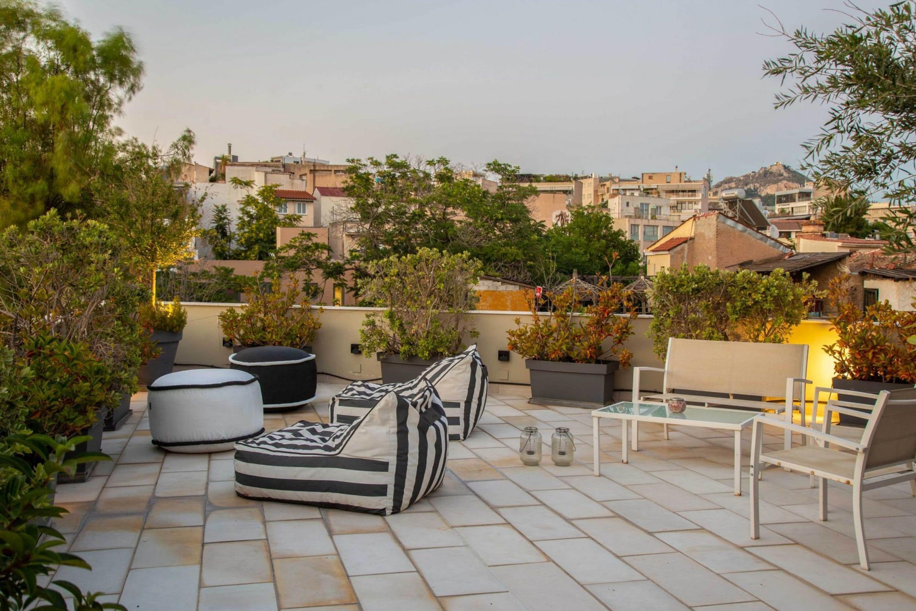 A rooftop patio with outdoor seating, potted plants, and a view of the cityscape.