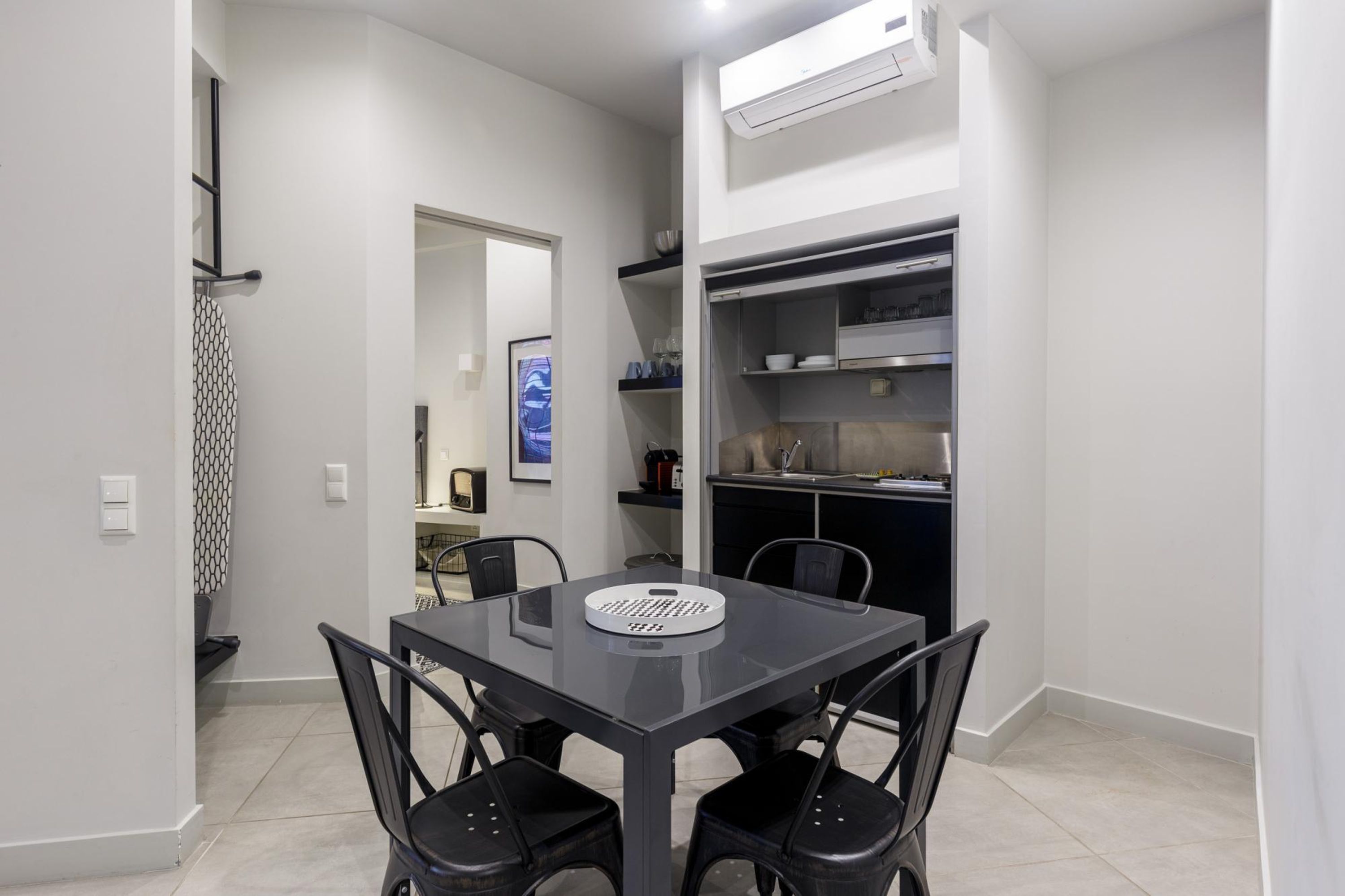 A compact kitchen with a dining area, featuring a black table and chairs, a built-in oven, and a white wall-mounted air conditioner.