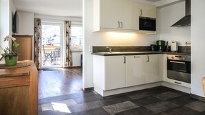 A modern kitchen with white cabinets, a microwave, and an oven. There is a wooden dining table with a potted plant. - Tauern Relax Lodges - Garden (Kaprun)