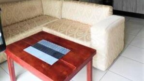 A living room with a sofa, a coffee table, and a television. There is a kitchen area with cabinets and a refrigerator. - 2 Bedroomed Apartment With En-suite and Kitchenette - 2066 (Harare)
