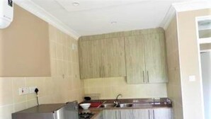 A compact kitchen with light wooden cabinets, a stainless steel refrigerator, and a sink. - 2 Bedroomed Apartment With En-suite and Kitchenette - 2066 (Harare)
